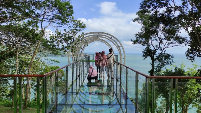 
 Pengunjung  berjalan di atas jembatan kaca sambil menikmati keindahan alam Mentari Ocean View. (Foto: Trinoto - Lensa Pacitan) 